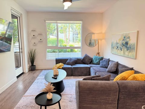 Spacious living room featuring a cozy L-shaped sofa, a full-size air mattress, and a 65" Smart TV with preloaded access to Netflix, Hulu, and Disney+, all set up for your enjoyment.