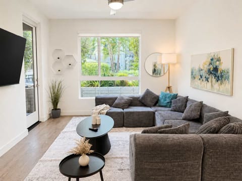 Spacious living room featuring a cozy L-shaped sofa, a full-size air mattress, and a 65" Smart TV with preloaded access to Netflix, Hulu, and Disney+, all set up for your enjoyment.