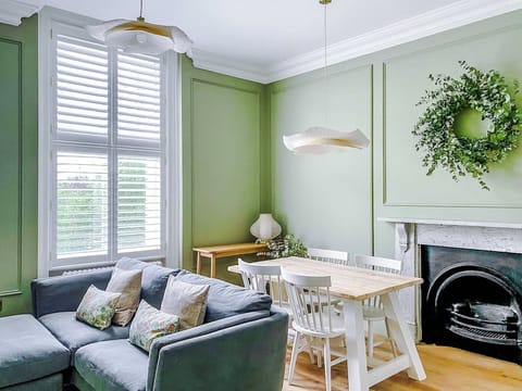 Muted tones, wood floors, and decorative fireplace set a refined tone. Dining table, cozy sofa, and natural light enhance the inviting, stylish atmosphere designed for relaxation and gatherings.