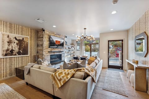 Open-concept living room with plush sectional, stone fireplace, and large windows