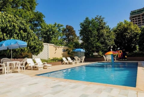 Lounge poolside under shady umbrellas and calm greenery.
