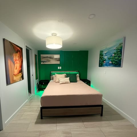 Queen bed, warm lighting and green accent wall; double nightstands with convenient bath access.