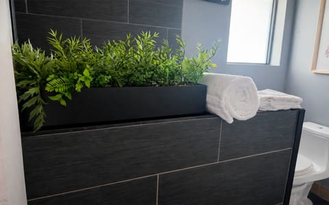 Thoughtful bathroom details in The Red Room, with fresh greenery, soft white towels, and modern dark tile finishes.