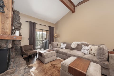 Unwind in your cozy living room with plush seating, rustic fireplace, and peaceful mountain views through the balcony doors.
