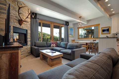 Unwind in your cozy living space with stone fireplace, plush seating, and mountain views through floor-to-ceiling windows.