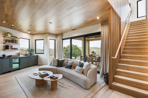 Bright and open living room featuring floor-to-ceiling windows, natural wood finishes, and seamless indoor-outdoor flow. A welcoming space designed for gathering and connection.