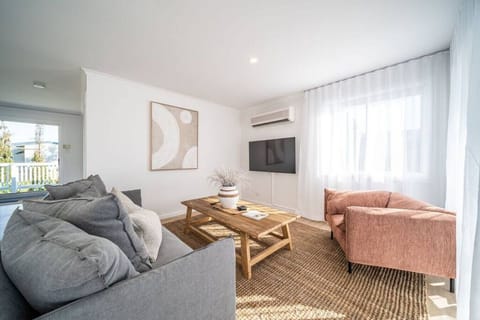 Unwind in the light-filled living area, where soft coastal tones, comfortable seating and a Smart TV create an inviting space for slow mornings and relaxed evenings after the beach.