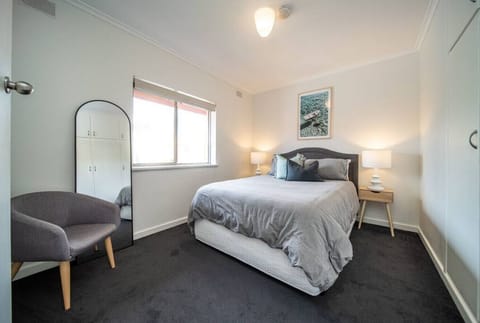 Bright and serene, this main bedroom features a plush queen bed, soft charcoal carpets, and a full-length mirror.