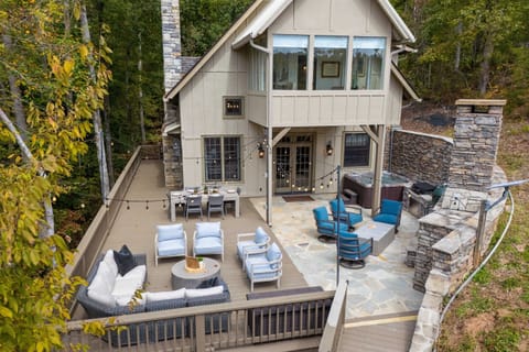 The aerial view of the back patio showcases plenty of seating, a large dining table, an outdoor fireplace, and a hot tub—perfect for relaxing and entertaining with beautiful lake views.
