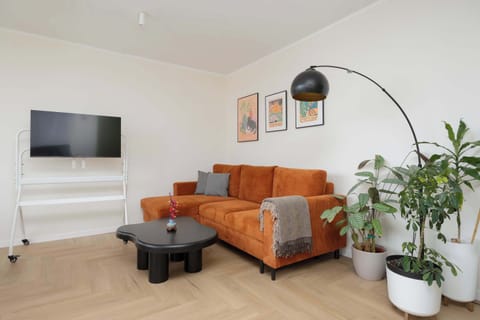 A bright and cozy living room featuring an orange sofa, TV, and large windows that fill the space with light.