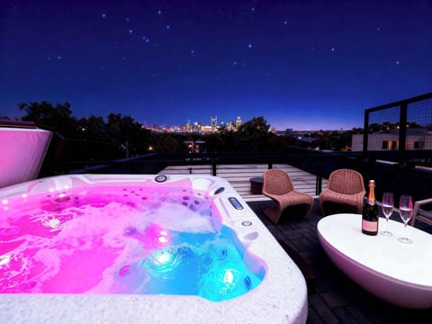 Pink and blue lights glow in the hot tub as the city sparkles above, the view that makes every soak feel like a celebration
