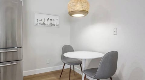 Cozy dining nook with a modern white table, sleek gray chairs, and a warm woven pendant light. The perfect spot for morning coffee or an intimate meal in a bright, minimalist setting.