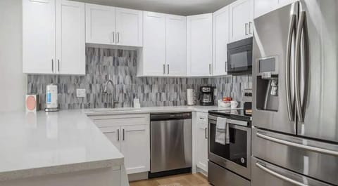 Contemporary kitchen with stainless steel appliances, sleek white cabinetry, and a stylish tile backsplash. Spacious countertops make it perfect for cooking, entertaining, or enjoying a relaxing meal at home.