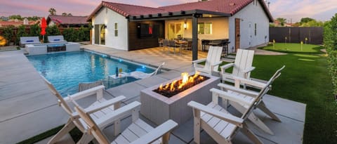 Twilight backyard hero — gas fire pit with Adirondack seating, outdoor TV under pergola, putting green & desert landscaping