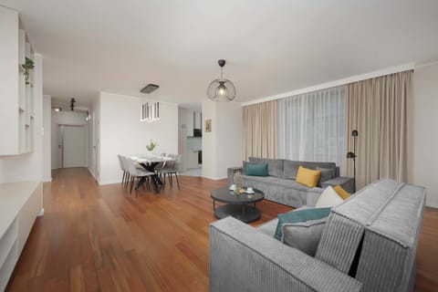A bright and spacious living room featuring elegant grey sofas, a large TV, and floor-to-ceiling windows that fill the space with natural light.