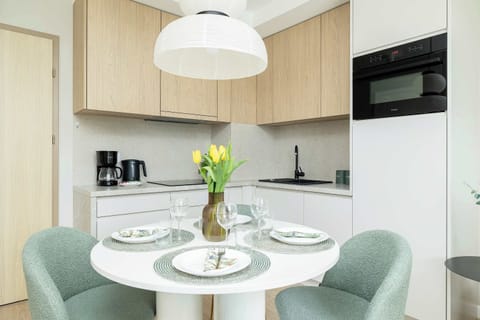 Bright dining nook featuring a round table, elegant pendant light, and green upholstered chairs. A vase with fresh flowers adds a cheerful touch.