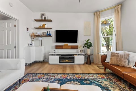 Bright and modern living room featuring a smart TV, electric fireplace, curated décor, and warm natural light.