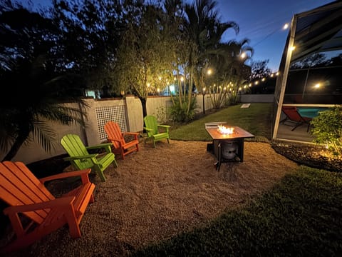 Twilight backyard with fire pit and bright chairs aglow under palms at dusk sky!