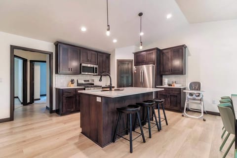 Bright kitchen view showcasing the island with comfortable stools and a convenient highchair, perfect for family meals or tailgate prep. Fully equipped with stainless steel appliances, it’s a stylish hub near Green Bay’s Lambeau Field.