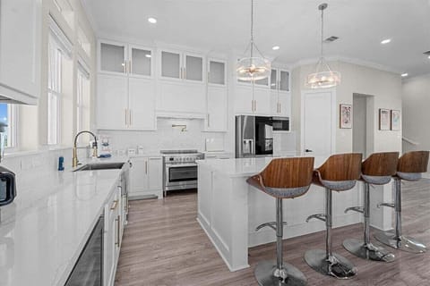 Modern white kitchen with stainless steel appliances, large island, and bar stools, perfect for cooking and entertaining.