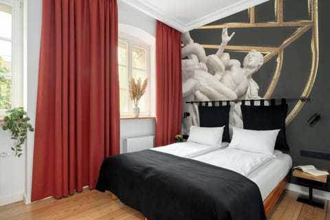 Stylish double room with a comfortable bed, elegant black-and-white bedding, and bold red curtains. The artistic wall mural featuring classical sculptures adds a unique character to the space.