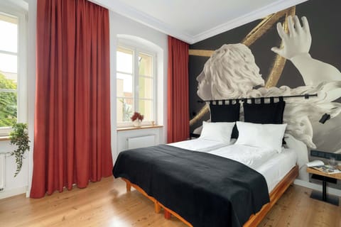 Stylish double room with a comfortable bed, elegant black-and-white bedding, and bold red curtains. The artistic wall mural featuring classical sculptures adds a unique character to the space.
