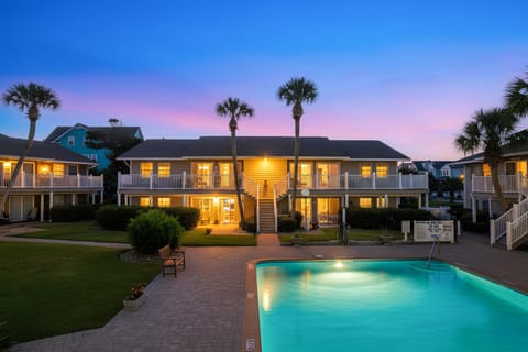 Stunning vacation property featuring illuminated accommodations, swaying palms, and a sparkling pool beneath vibrant sunset skies.