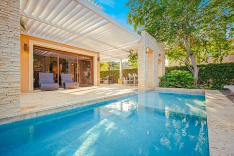 Golden sunlight dances on turquoise water beside modern stone walls and lush greenery—pure tropical tranquility in motion.