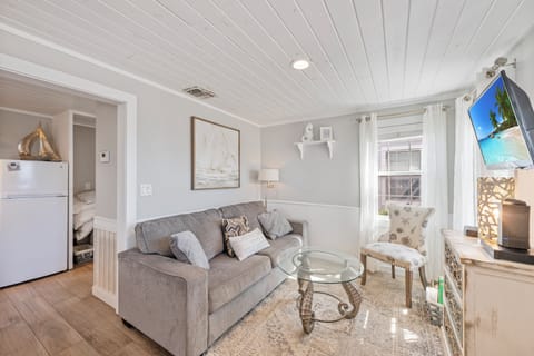 Unwind in your cozy living room with soft gray furnishings, elegant coastal artwork, and natural light streaming through crisp white curtains.