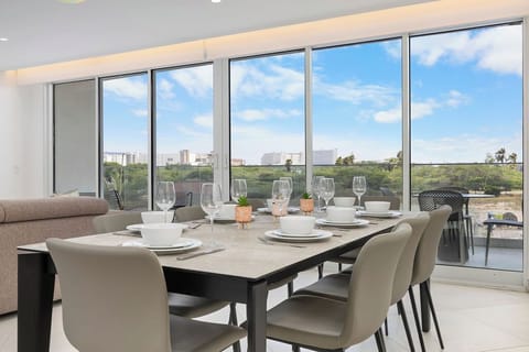 Gather around this elegant dining table set for six with sweeping views of lush greenery and distant cityscape through floor-to-ceiling windows.