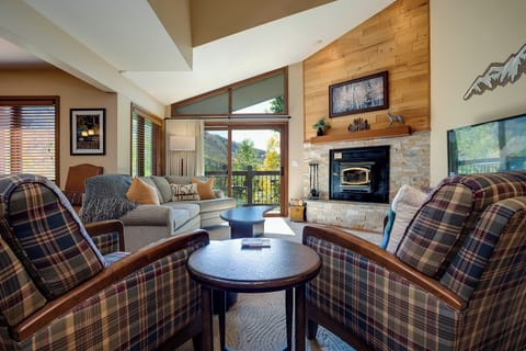 Cozy up by your stone fireplace in this inviting living room, where plaid chairs and mountain views create the perfect alpine retreat.