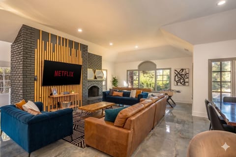 Stylish, sunlit living space with a statement fireplace, cozy seating, and a large TV—perfect for relaxing or movie nights. ✨📺