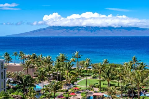 Panoramic ocean views to Molokai rise beyond the turquoise shoreline, with Honua Kai tropical pools, palms, and gardens creating a postcard-perfect foreground. HKK-829
