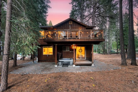 Back exterior view of the cabin, featuring a hot tub and a forest backdrop.