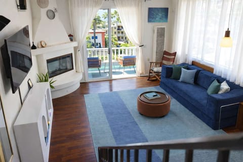 A bright coastal modern living room featuring a cozy sofa, an aesthetic fireplace, and sun-drenched balcony with outdoor views.