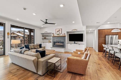 The room centers around a modern, gas-burning fireplace set in a sleek grey tile surround with a natural wood mantel.