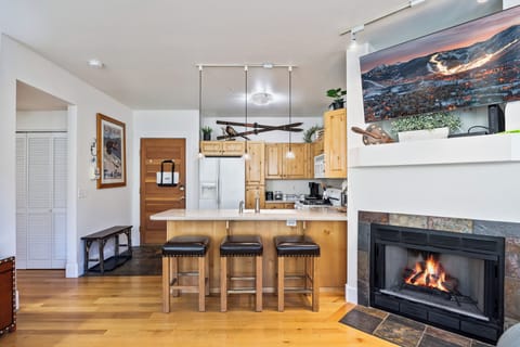 A cozy and functional kitchen featuring natural wood cabinetry, a large island with seating, and a charming fireplace that adds warmth and ambiance. Perfect for cooking, entertaining, or enjoying morning coffee by the fire.