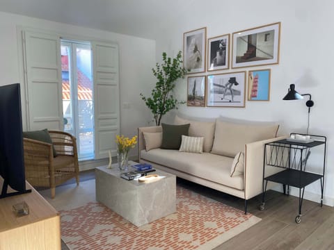 A light-filled living room with a sofa, artwork, and patterned floor tiles.