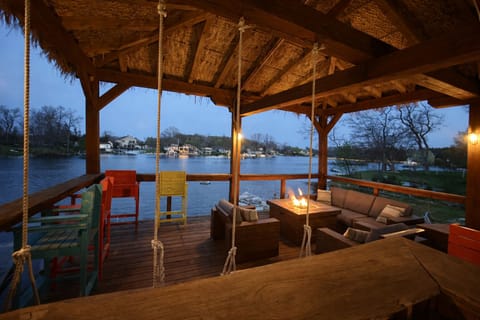 Covered lakefront tiki deck with seating, lights, and stunning sunrise views