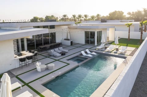 An elevated view of the resort-style backyard in the morning sun, showcasing the pool, spa, outdoor bar, and various lounge areas.