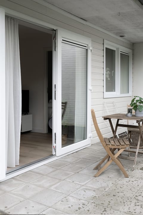 Cozy patio with folding wooden chairs and a small table, perfect for morning coffee. Sliding door leads directly to the bright and modern interior.