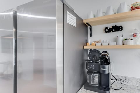 Start your day right with this convenient coffee nook, showcasing a modern coffee maker alongside a spacious fridge and well-organized pantry essentials, ready for your favorite morning brews.