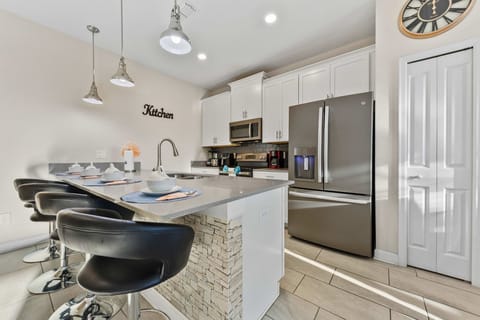 Modern kitchen with quartz countertops, stainless appliances, and white shaker cabinets-plus a stone-accent breakfast bar with seating for four under chic pendants.