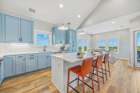 Picture yourself cooking in this bright, open kitchen with sleek blue cabinetry, a spacious island, and natural light streaming through windows overlooking greenery—your perfect vacation retreat awaits.