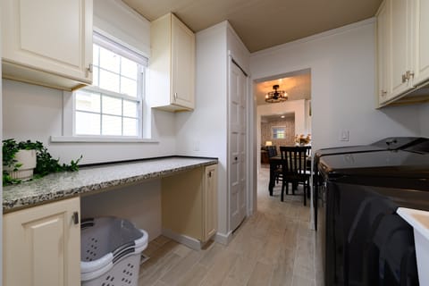 Laundry area with washer, dryer, ironing board, and laundry soap for guest convenience.