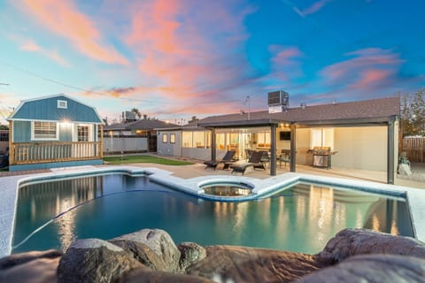 Sunset colors reflecting across the backyard pool create a relaxing evening scene, with the connected spa, lounge seating, and patio lights inviting you to unwind poolside as the sky shifts from blue to warm pink.