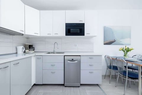Fully equipped white kitchen with built-in appliances and a small dining area.