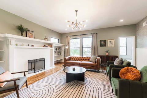 Bright, stylish living room with cozy leather sofa, green armchairs, and modern décor. Features a fireplace, large windows for natural light, and a chic coffee table—perfect for relaxing or entertaining guests.
