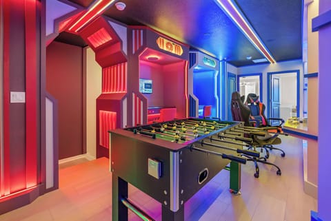 Welcome to a lively game room featuring neon lights and a stylish foosball table, perfect for friendly competition. With modern gaming chairs and eye-catching decor, this space offers fun and relaxation for everyone.