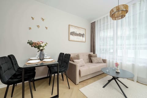 A bright living room with a beige sofa, black dining chairs, and a modern light fixture. The space feels cozy and elegant with soft lighting.